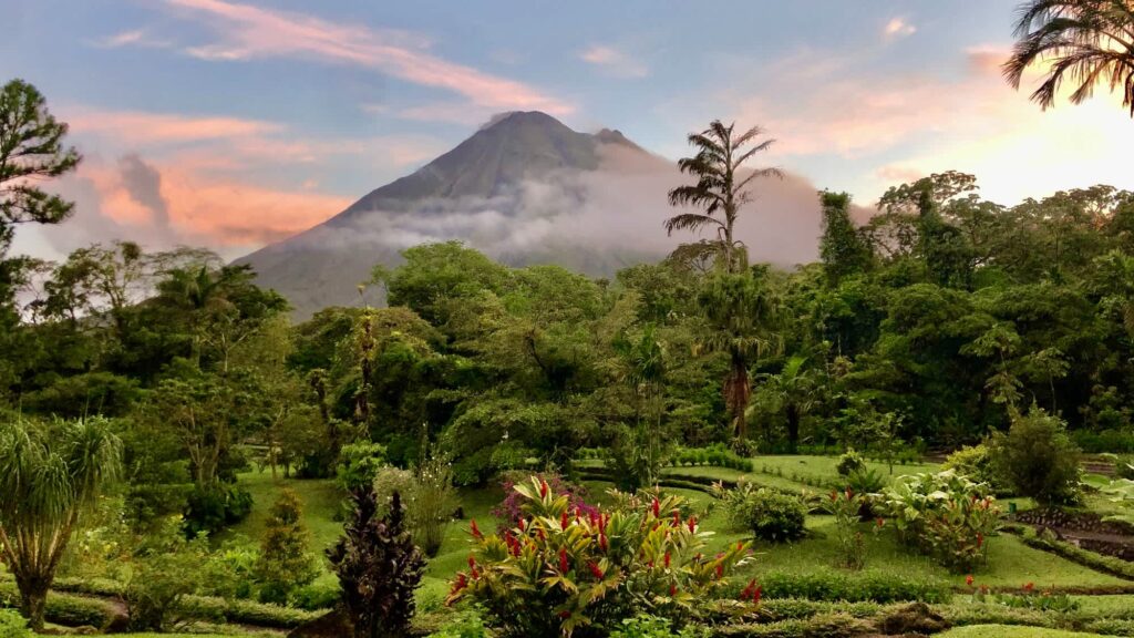 A spectacular view of the Arenal Volcano, located in Costa Rica's Northern Zone, captured from a distance. The image showcases the majestic cone-shaped volcano rising above the lush green landscape.