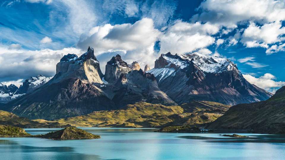 A scenic view of Chile's Patagonia region captured during a fjords cruise. The image showcases a walk towards the Torres del Paine mountain range, with a stunning blue lake visible in the foreground.